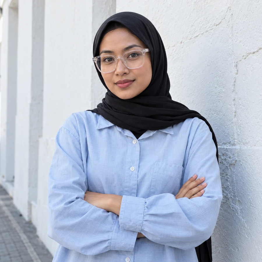 Hijab hitam dan kacamata kotak bening di depan dinding putih
